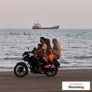 Cargo and service vessels line the horizon as people ride a motorcycle along the Strait of Hormuz, off Bandar Abbas, Iran, May 31.